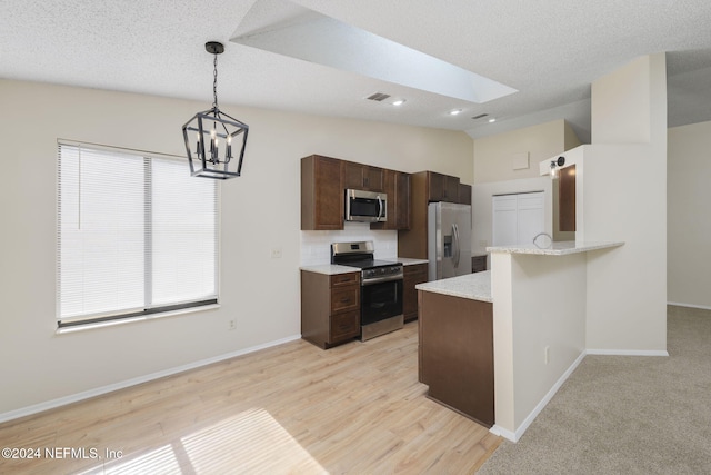 kitchen featuring a notable chandelier, kitchen peninsula, lofted ceiling with skylight, pendant lighting, and appliances with stainless steel finishes