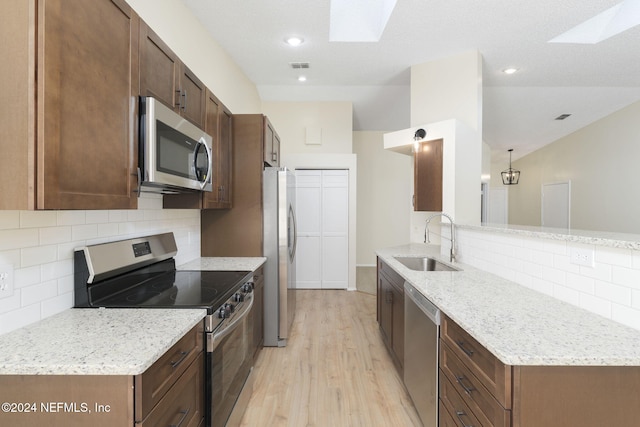 kitchen with a skylight, sink, stainless steel appliances, and light hardwood / wood-style floors