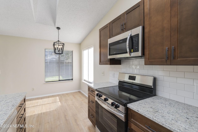 kitchen with stainless steel appliances, light stone counters, a notable chandelier, decorative light fixtures, and vaulted ceiling