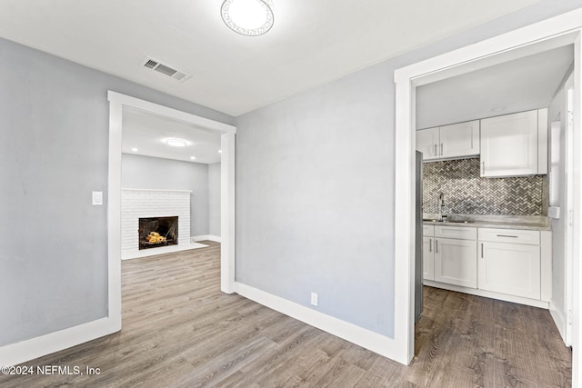 kitchen featuring sink, decorative backsplash, a fireplace, white cabinets, and light wood-type flooring