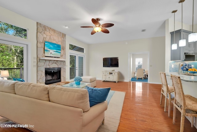 living area with ceiling fan, a stone fireplace, visible vents, baseboards, and light wood-style floors