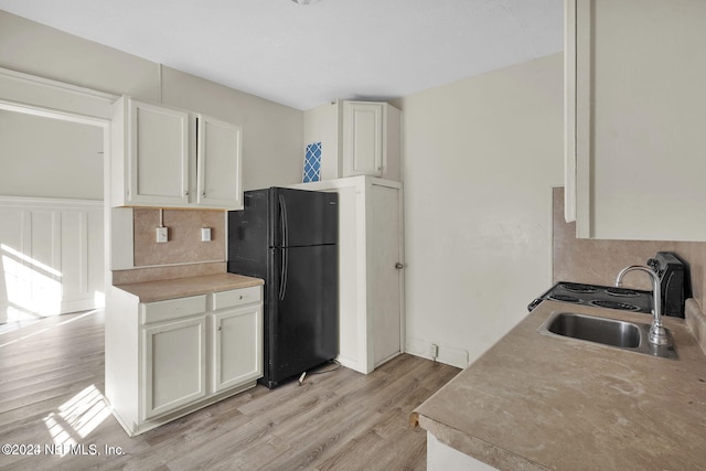 kitchen with white cabinets, black refrigerator, sink, light hardwood / wood-style flooring, and decorative backsplash