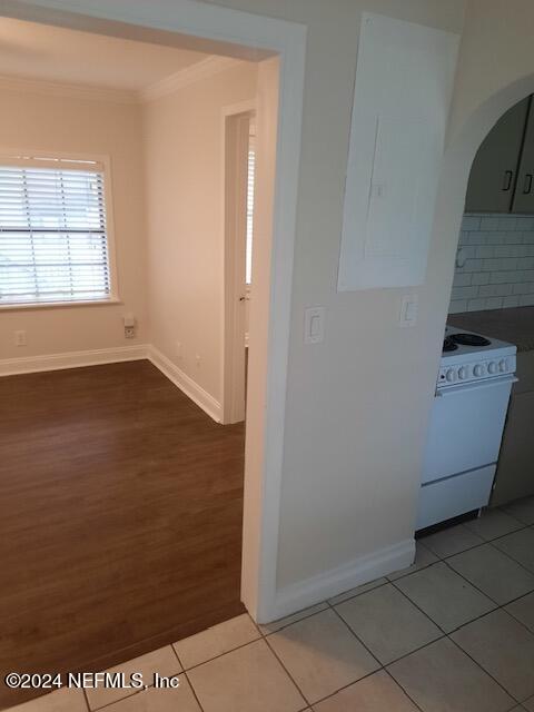 interior space featuring electric stove, decorative backsplash, hardwood / wood-style floors, and ornamental molding