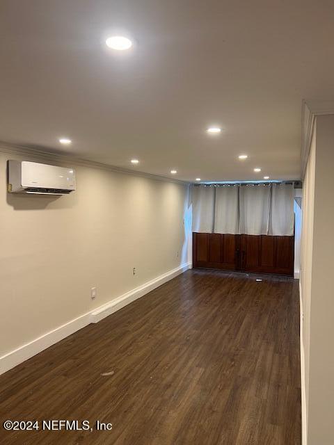 basement with ornamental molding, dark wood-type flooring, and a wall mounted AC