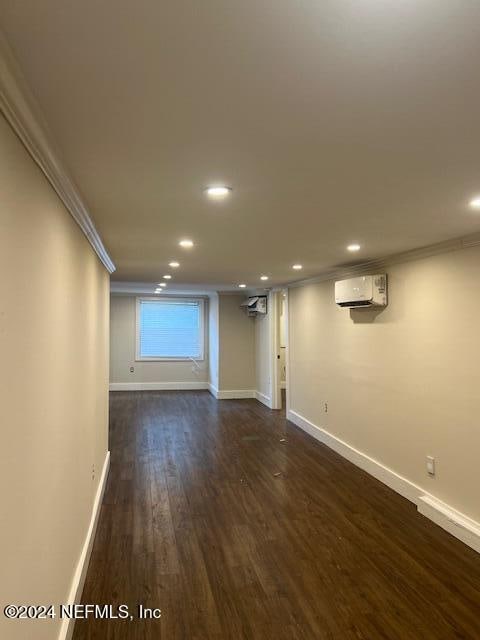 basement with dark wood-type flooring, a wall unit AC, and crown molding