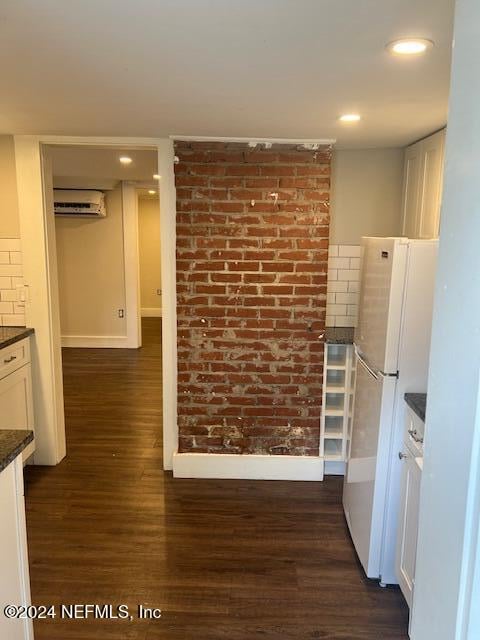 kitchen featuring white cabinets, white refrigerator, dark hardwood / wood-style floors, dark stone countertops, and a wall unit AC