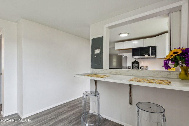 kitchen with electric panel, appliances with stainless steel finishes, dark hardwood / wood-style flooring, white cabinetry, and a breakfast bar area