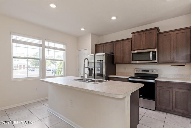 kitchen featuring appliances with stainless steel finishes, sink, light tile patterned floors, and an island with sink