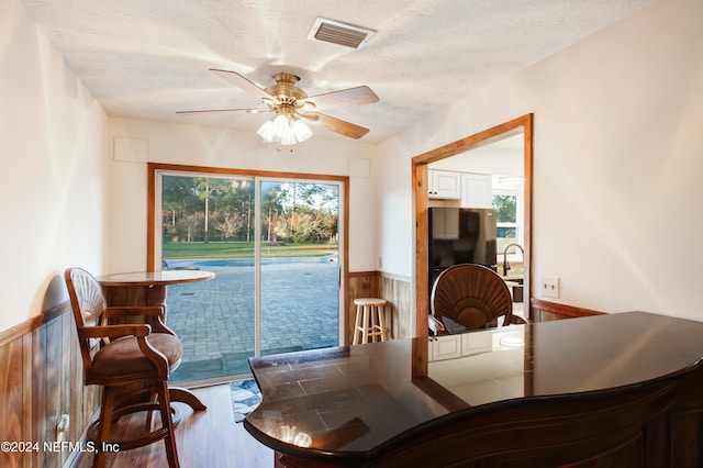 dining area with ceiling fan, wood walls, wood-type flooring, and a textured ceiling