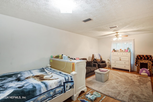 bedroom with ceiling fan, wood-type flooring, and a textured ceiling