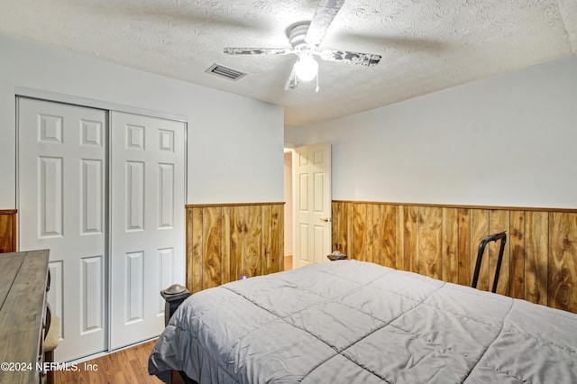 bedroom with ceiling fan, wooden walls, a textured ceiling, and hardwood / wood-style flooring