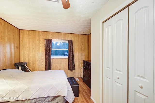 bedroom featuring wood walls, ceiling fan, a textured ceiling, light hardwood / wood-style floors, and a closet