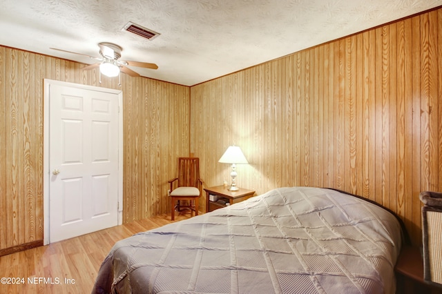 bedroom featuring a textured ceiling, ceiling fan, wood-type flooring, and wood walls