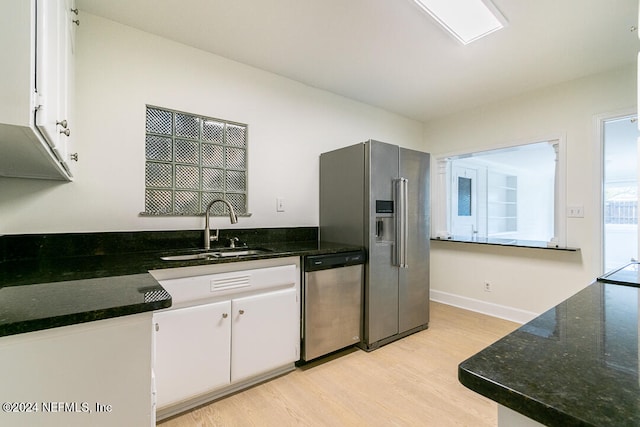 kitchen featuring dark stone counters, sink, appliances with stainless steel finishes, light hardwood / wood-style floors, and white cabinetry