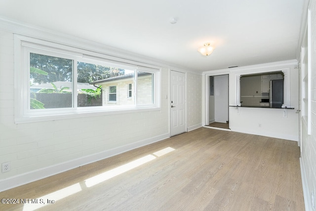 unfurnished living room with light hardwood / wood-style floors, plenty of natural light, and brick wall