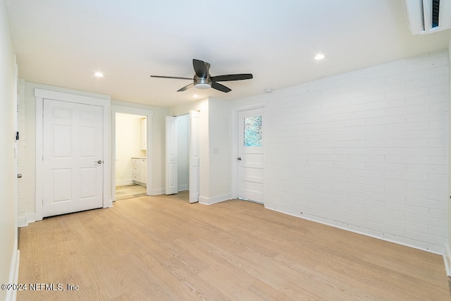 unfurnished bedroom with ensuite bath, ceiling fan, light hardwood / wood-style floors, and brick wall