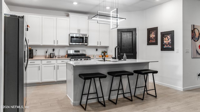 kitchen featuring stainless steel appliances, decorative light fixtures, a center island with sink, white cabinetry, and a breakfast bar area