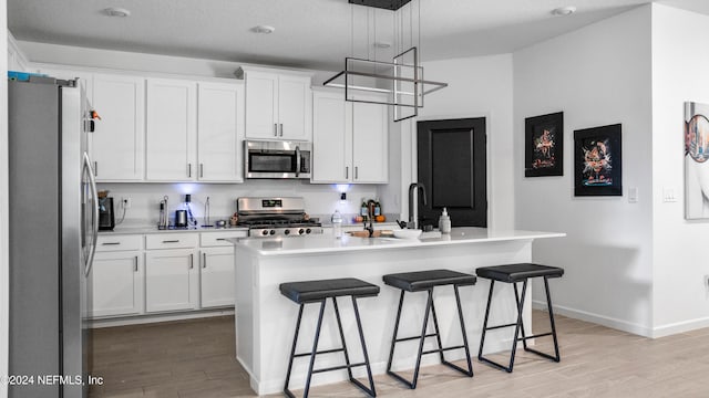 kitchen featuring appliances with stainless steel finishes, a kitchen island with sink, light hardwood / wood-style floors, white cabinetry, and hanging light fixtures