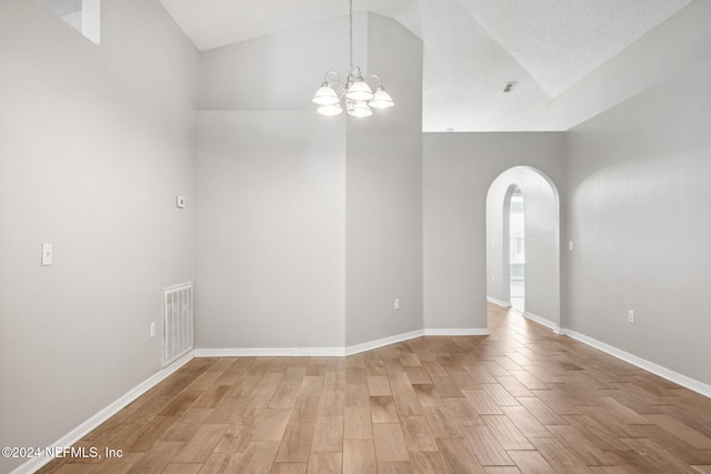 empty room with high vaulted ceiling, a chandelier, a textured ceiling, and light wood-type flooring