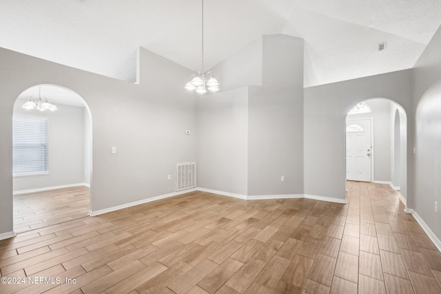 empty room featuring light hardwood / wood-style flooring, high vaulted ceiling, and an inviting chandelier