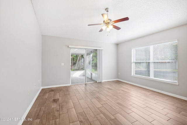 empty room with ceiling fan, light wood-type flooring, and a textured ceiling