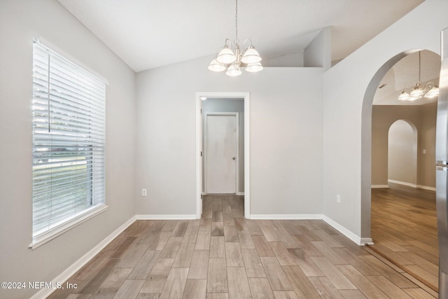 empty room featuring hardwood / wood-style floors, lofted ceiling, and an inviting chandelier