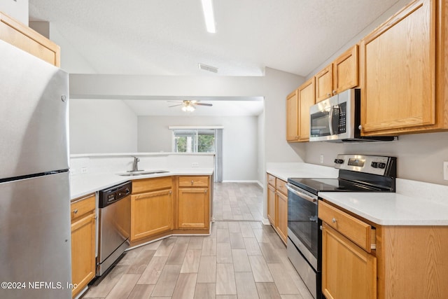 kitchen with kitchen peninsula, appliances with stainless steel finishes, light wood-type flooring, sink, and lofted ceiling