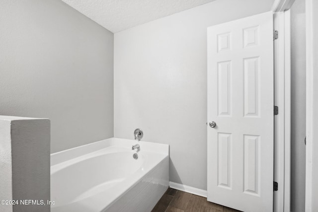 bathroom with hardwood / wood-style floors, a textured ceiling, and a tub