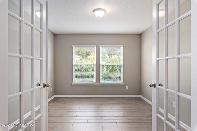 empty room featuring french doors, a textured ceiling, and wood-type flooring