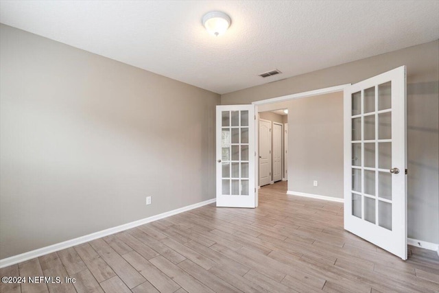 spare room featuring french doors, a textured ceiling, and light hardwood / wood-style floors