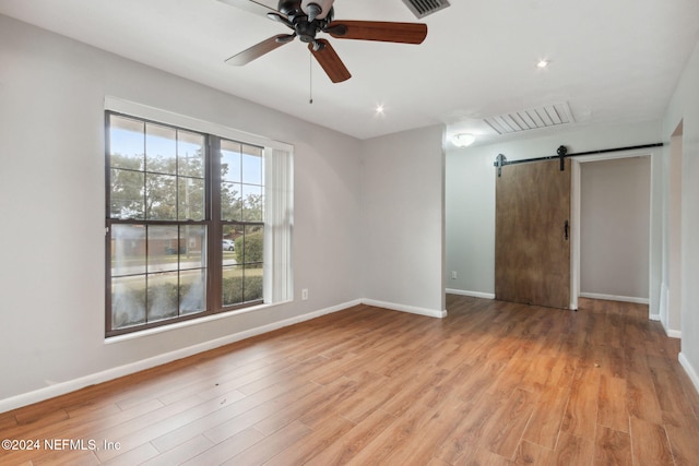 unfurnished room featuring ceiling fan, a barn door, and light hardwood / wood-style flooring