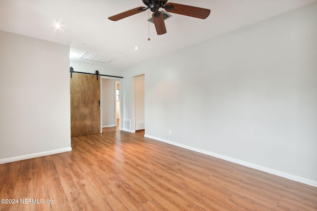 spare room with ceiling fan, a barn door, and light hardwood / wood-style flooring