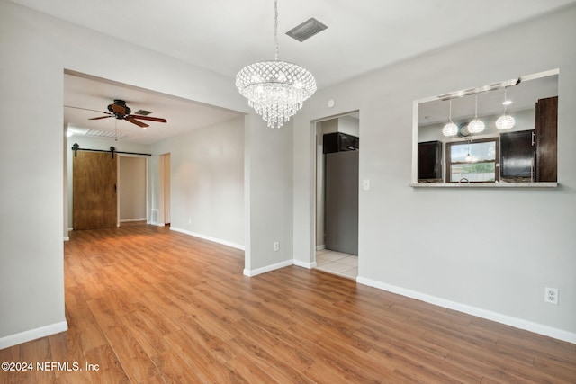 empty room with ceiling fan with notable chandelier, a barn door, and light hardwood / wood-style flooring