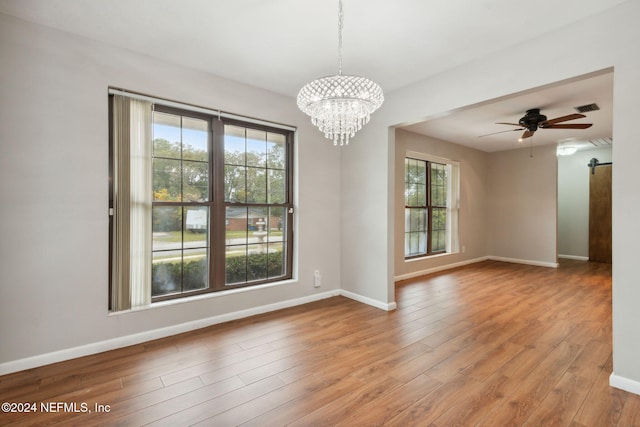 unfurnished room with a barn door, light hardwood / wood-style flooring, and ceiling fan with notable chandelier