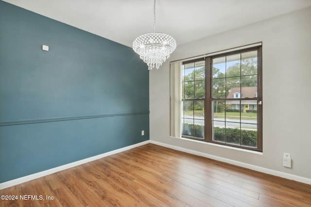 spare room with wood-type flooring and an inviting chandelier