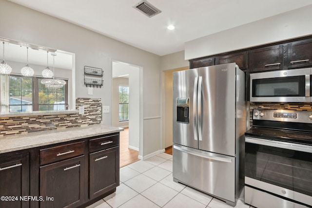 kitchen with light stone countertops, decorative light fixtures, dark brown cabinets, light tile patterned floors, and appliances with stainless steel finishes