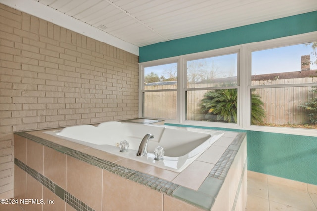 bathroom with tile patterned floors, tiled tub, and brick wall