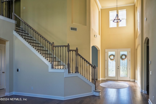 foyer entrance with french doors, dark hardwood / wood-style flooring, crown molding, a chandelier, and a high ceiling