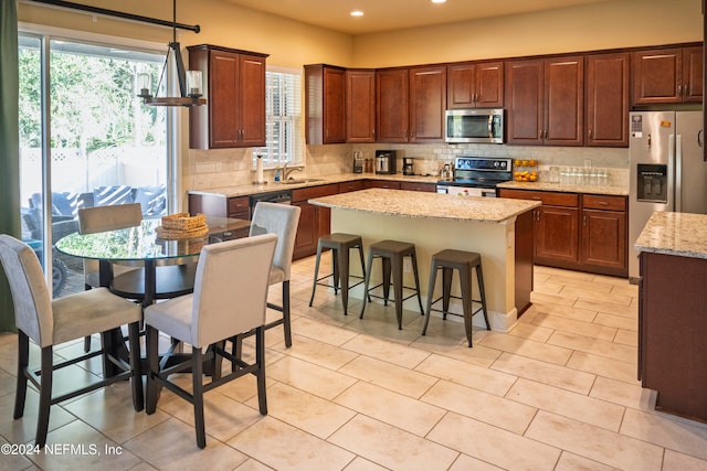 kitchen with light stone countertops, decorative light fixtures, decorative backsplash, a kitchen island, and appliances with stainless steel finishes