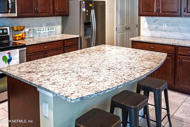 kitchen with a center island, backsplash, light stone countertops, appliances with stainless steel finishes, and a kitchen bar