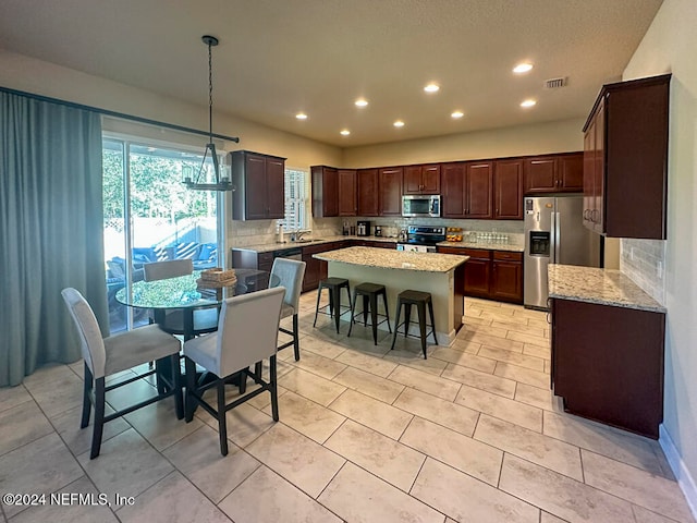 kitchen with appliances with stainless steel finishes, a center island, hanging light fixtures, and backsplash