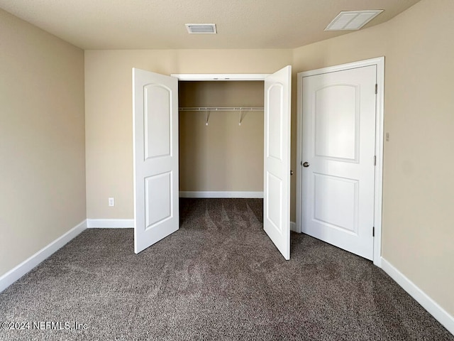 unfurnished bedroom with dark colored carpet and a closet