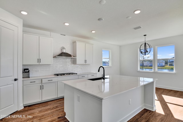 kitchen with sink, light stone counters, dark hardwood / wood-style floors, a center island with sink, and white cabinets