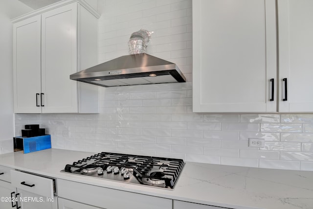 kitchen featuring backsplash, light stone counters, wall chimney range hood, white cabinetry, and stainless steel gas stovetop