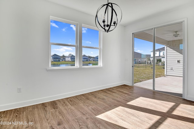 unfurnished dining area featuring wood-type flooring, ceiling fan with notable chandelier, and a water view