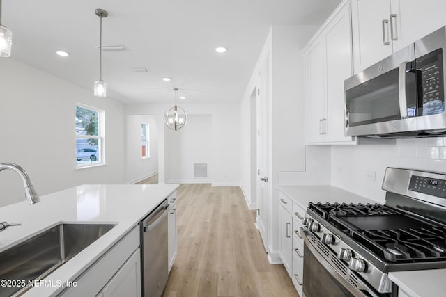 kitchen featuring sink, hanging light fixtures, stainless steel appliances, tasteful backsplash, and white cabinets