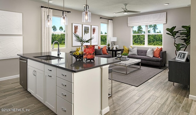 kitchen featuring light wood-type flooring, sink, decorative light fixtures, white cabinets, and an island with sink