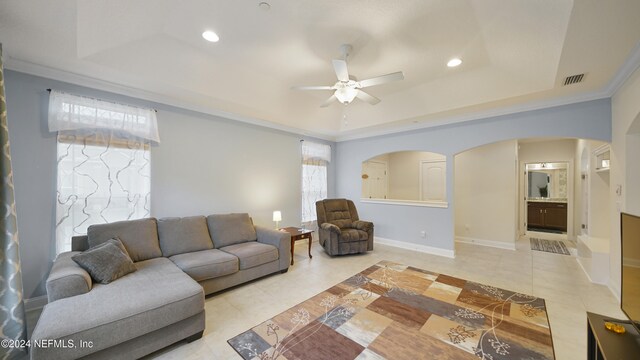 tiled living room with a raised ceiling, ceiling fan, and crown molding