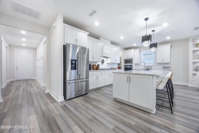 kitchen with white cabinetry, light stone countertops, decorative light fixtures, a kitchen island with sink, and appliances with stainless steel finishes