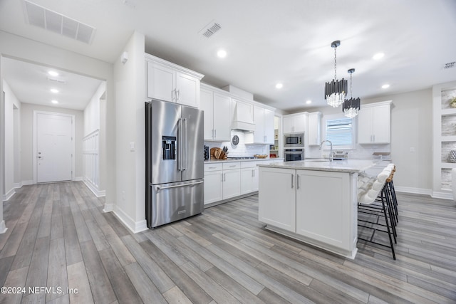 94 Hickory Pine Dr, Saint Augustine, FL 32092 - kitchen featuring stainless steel appliances, custom range hood, light wood-type flooring, an island with sink, and white cabinetry